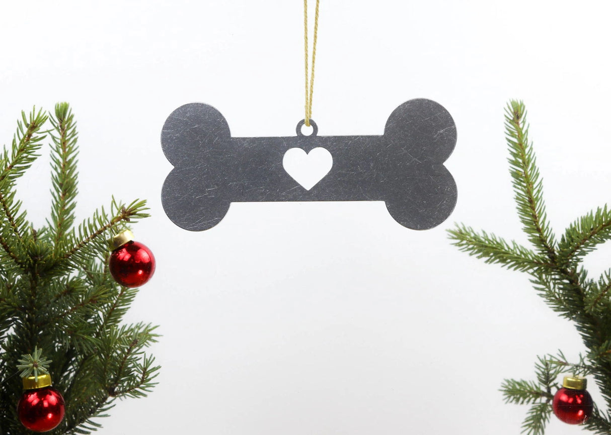 Dog bone metal ornament with heart cutout, hanging from a Christmas tree branch.