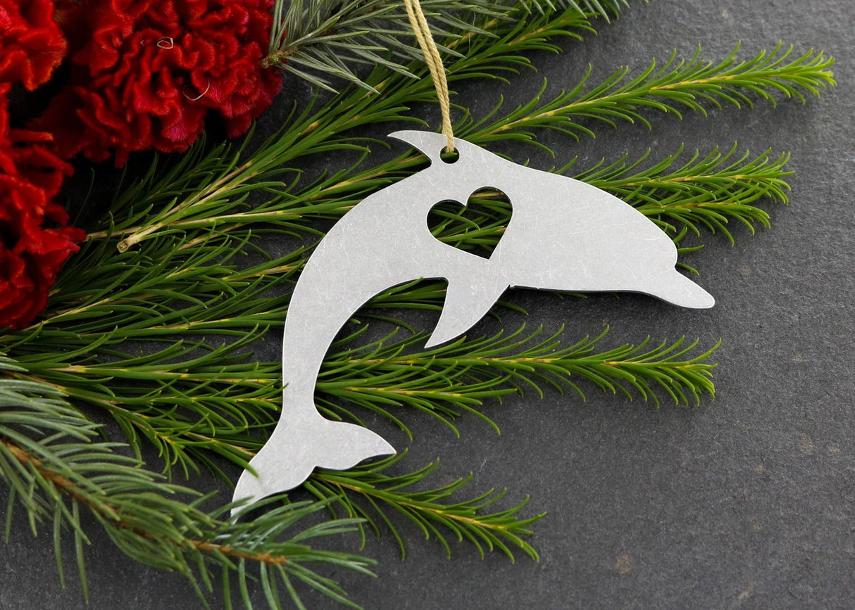 Dolphin metal ornament with heart cutout, surrounded by greenery and red flowers.