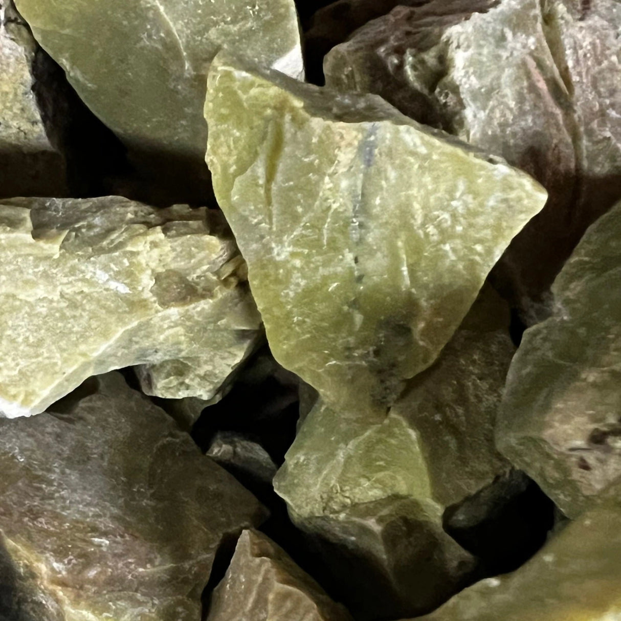 Green Opal Raw - Close-up of a cluster of raw green opal stones with irregular shapes and sizes. The stones exhibit a translucent green color with variations in shade and internal fractures.