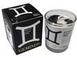 Candle with Gemini zodiac design next to its packaging on a light gray background