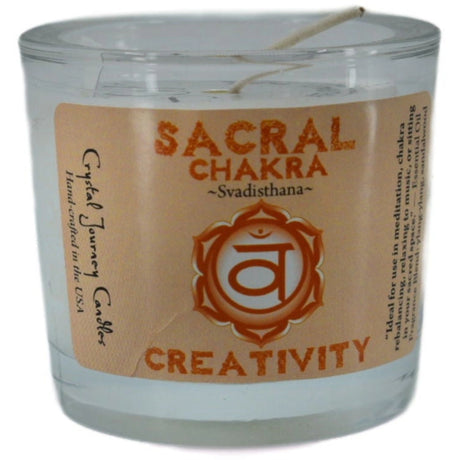 Orange votive candle with the words "SACRAL CHAKRA," "SVADISTHANA," and "CREATIVITY" printed on it. The candle is surrounded by a white label with additional information about its use for meditation and chakra balancing.