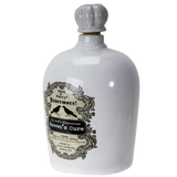 A white ceramic bottle with a gray ribbed stopper, featuring a vintage-style label for 'Ravenmore' 'Raven's Cure' with black raven silhouettes and ornate detailing.