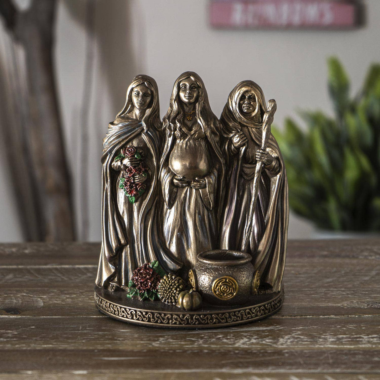 Bronze figurine of three women on a wooden surface with a blurred background