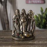 Bronze figurine of three women on a wooden surface with a blurred background