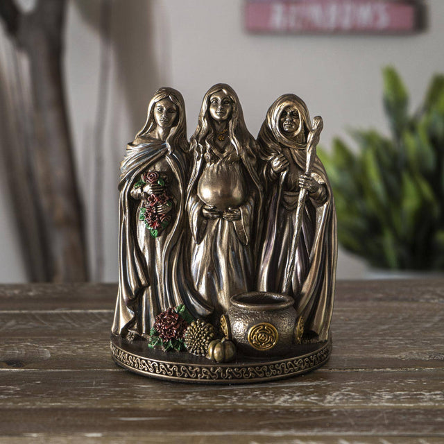 Bronze figurine of three women on a wooden surface with a blurred background