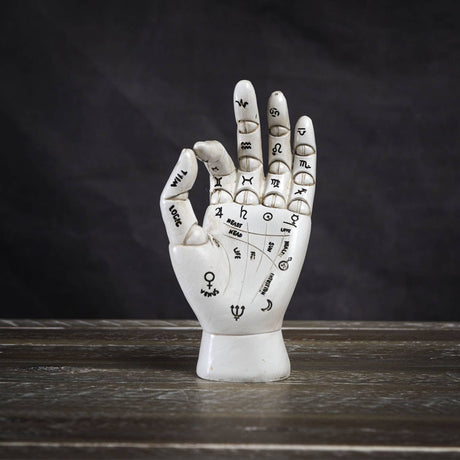 Decorative palmistry hand sculpture on a wooden surface with a dark background