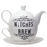 White ceramic teapot and matching teacup with saucer, featuring black gothic-style text reading 'WITCHES BREW' with decorative swirls and a pentagram symbol.