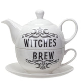 A white ceramic teapot and matching teacup with saucer set, featuring black gothic-style text reading 'WITCHES BREW' with decorative swirls, a pentagram, and crescent moon motif.