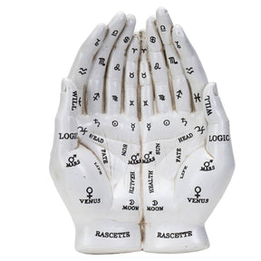 A white decorative model of two hands facing each other, printed with black astrological and zodiac symbols and labels such as Venus, Moon, Mars, Jupiter, Saturn, Pluto, and Rascette.
