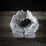 A pair of white sculptural hands with astrological and zodiac markings, holding a black car key fob on a rustic wooden surface against a dark background.