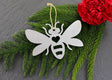 Bee metal ornament with heart cutout, surrounded by greenery and a red flower.