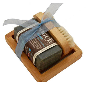 Wooden soap dish with a bar of green goat milk soap and a small, round brush. The soap bar has a label that reads "Bogue," "Greasemonkey," and "Organic Coconut." The soap dish is tied with a blue ribbon.