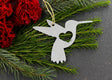 Hummingbird metal ornament with heart cutout, surrounded by greenery and red flowers.