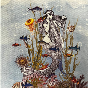 Mermaid canvas magnet with illustration of a mermaid surrounded by sea creatures and coral reef.