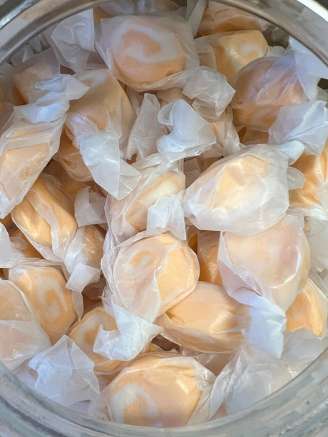 Orange Salt Water Taffy - Orange candy piece with a white swirl wrapped in wax paper 