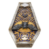 A coffin-shaped decorative lantern or candle holder featuring a black bat perched on a gold crescent moon, with a small white owl at the bottom and a silver metal cup at the top, set against a blue and gold patterned background.
