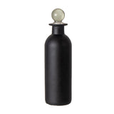 A matte black bottle with a spherical pale green glass stopper on a white background.
