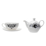A white ceramic teapot and matching cup with saucer, both decorated with black gothic-style cat illustrations and text reading 'PURR-FECT' and 'BREW'.