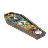 A coffin-shaped decorative tray or dish with a dark wood-look frame and a colorful gothic-themed lid featuring a black butterfly, a large eye motif, a spider, a pentagram, and a small silver bowl.